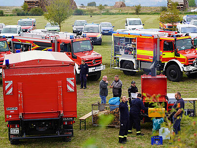 Auf einer Wiese sind verschiedene RedMogs aufgestellt, daneben unterhalten sich Menschen 
