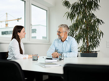 Zwei Personen sitzen in einem Besprechungsraum im Gespräch an einem Tisch.