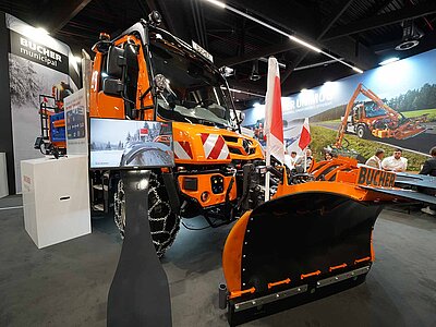 Ein orangefarbener Unimog auf einem Messestand in einer Halle. 