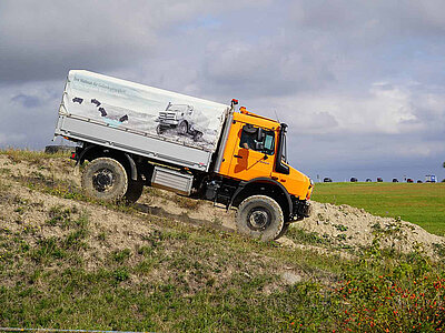 Ein oranger Unimog fährt einen Berg herunter
