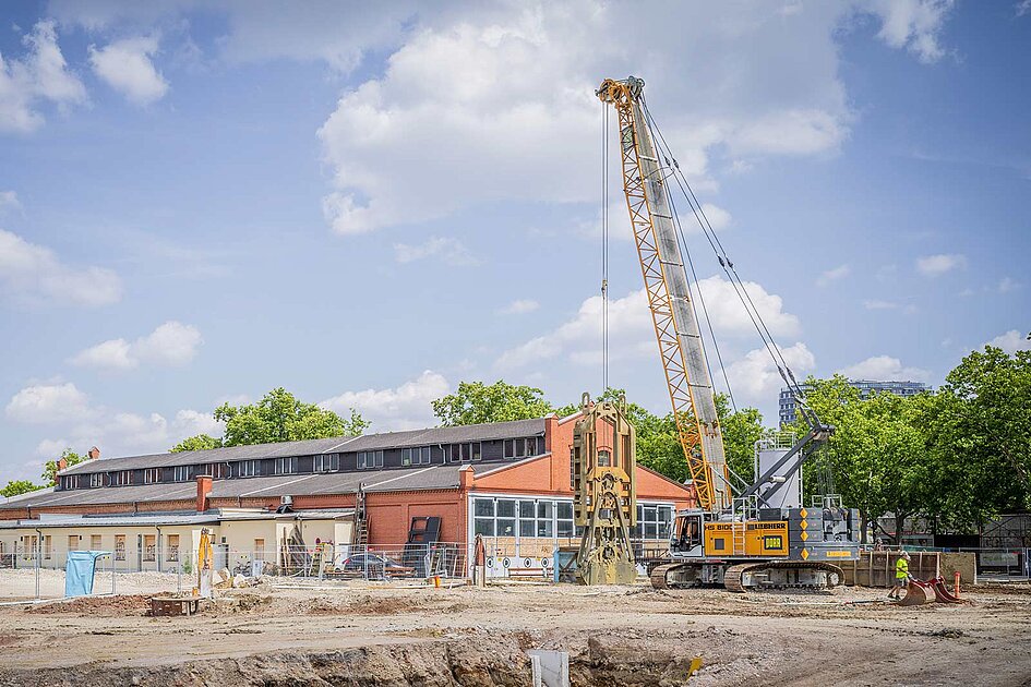Ein Liebherr Seilbagger auf einer urbanen Baustelle unter blauem Himmel.
