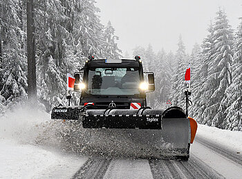 Ein Unimog mit Schneeschild von frontal bei der Arbeit auf der Straße.