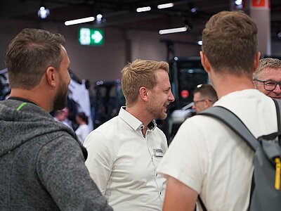 Drei Menschen im Gespräch auf einem Messestand. 