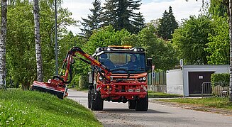 Ein orangefarbenes Fahrzeug mit Anbau neben einer Rasenfläche.