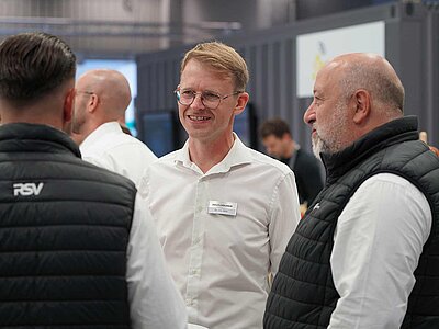 Drei Menschen im Gespräch auf einem Messestand.
