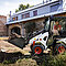 Bobcat Kompakt-Knicklader befördert eine Schaufel Erde vor einem Haus