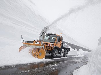 Unimog mit gelber Zaugg-Schneefräse räumt hohe Schneemassen am Straßenrand