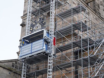 Der Bauaufzug ist an einem Gerüst vor dem Kirchturm installiert und erleichtert den Materialtransport während der Bauarbeiten
