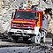 Ein roter Unimog auf unebenem Terrain in einem Steinbruch. 