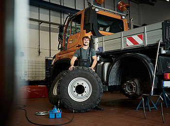 Ein Servicetechniker steht mit einem Reifen vor einem Unimog.
