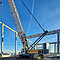 Ein gelber Raupenkran auf einer Baustelle einer Halle unter blauem Himmel.