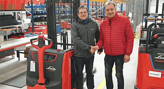wei Männer im Lager schütteln sich die Hand zwischen zwei neuen Linde-Flurförderzeugen in Lagerhalle