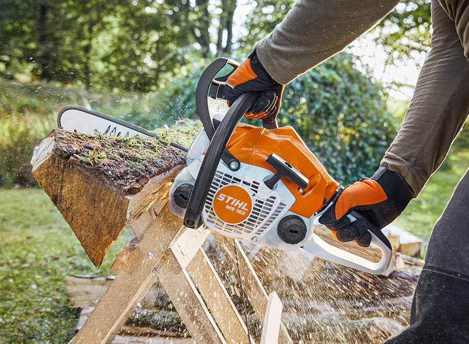 Eine Mensch schneidet Holz mit einer orange-weißen Motorsäge im Grünen.