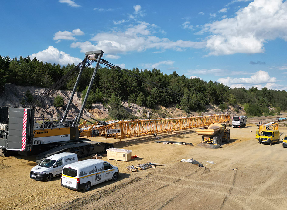 Ein gelber Raupenkran LR bei der Montage auf einer Baustelle unter blauem Himmel.