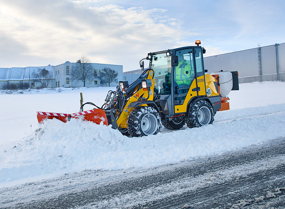 Ein gelber Radlader mit Schneeschild wird zum Schneepflügen auf einer verschneiten Straße eingesetzt.