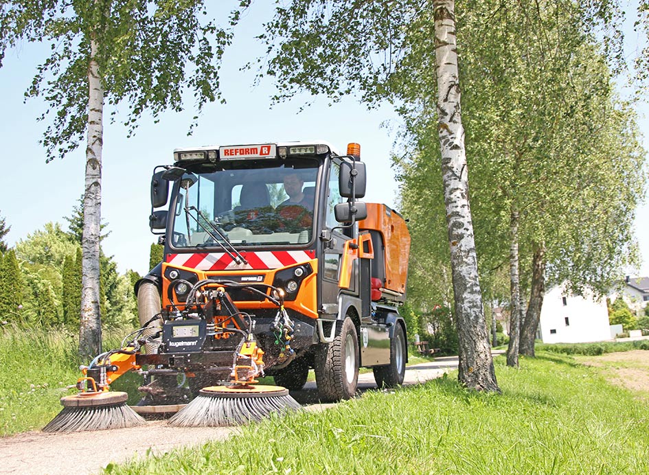 Ein orangefarbenes Fahrzeug mit Kehrmaschinenanbaugerät