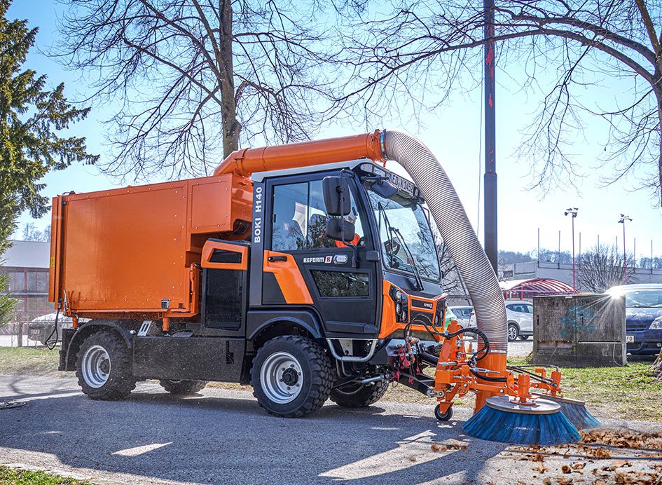 Ein orangefarbenes Trägerfahrzeug mit Anbaugerät unter blauem Himmel.