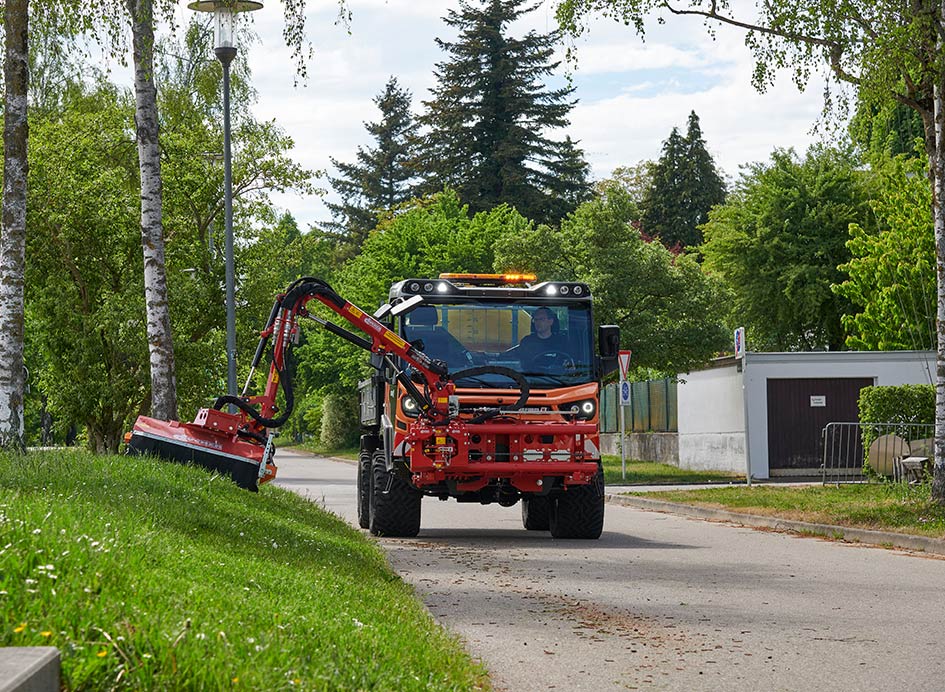 Ein orangefarbenes Fahrzeug mit Anbau neben einer Rasenfläche.