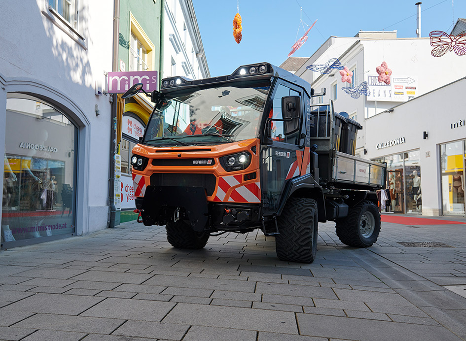 Ein orangefarbenes Kommunalfahrzeug in einer Fußgängerzone.