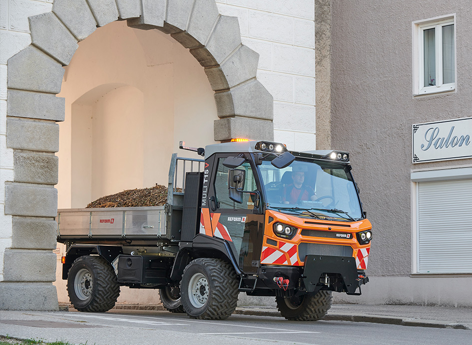 Ein orangefarbenes Fahrzeug mit Kipper bei kommunalen Arbeiten.