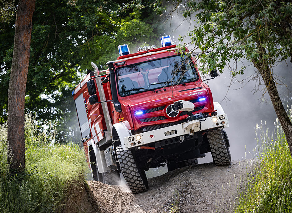 Ein rot-weißer Unimog in bewaldetem Gelände bei Löscharbeiten.