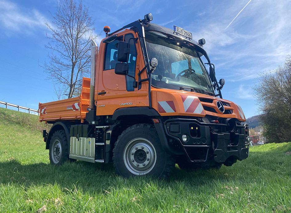 Ein orangener Unimog Geräteträger auf grünem Rasen. 