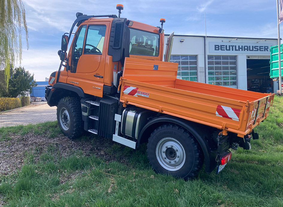 Ein oragenfarbener Unimog Geräteträger bei der Auffahrt einer Anhöhe auf einen Hof.